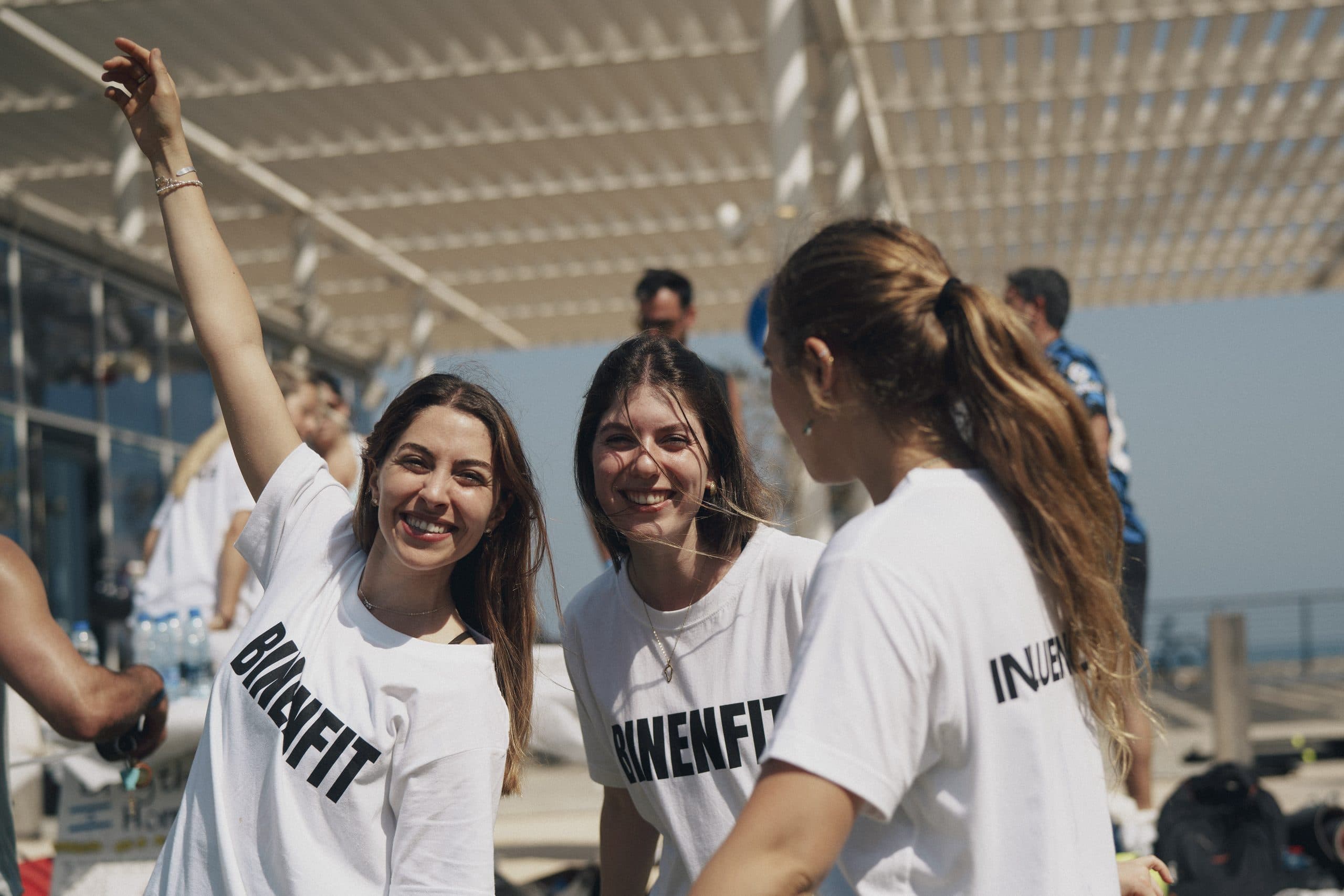 Three friends in BINENFIT shirts laughing together at a community event